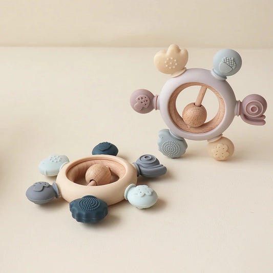 Two MimiAnneau™ silicone and wood baby teething rings in pastel colors with textured shapes.