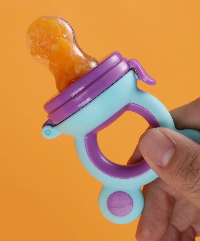 TétineSaveur Trio silicone baby feeder with orange fruit puree held by a hand against an orange background